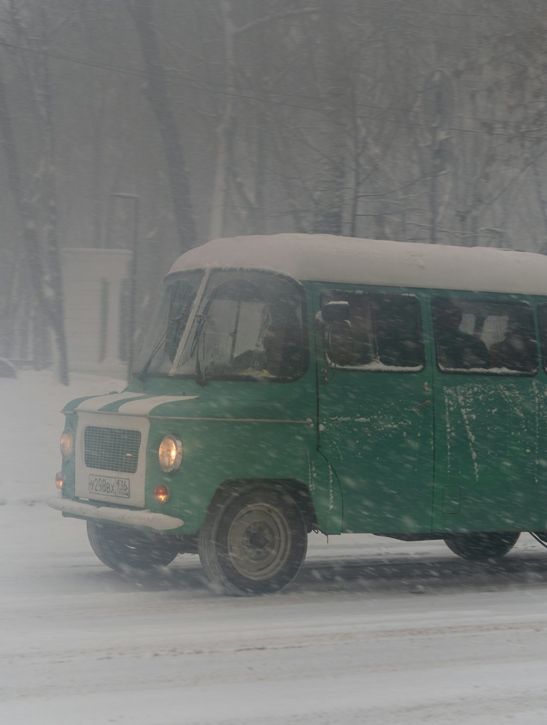 En grønn vintage buss kjører langs en snødekt vei om vinteren.