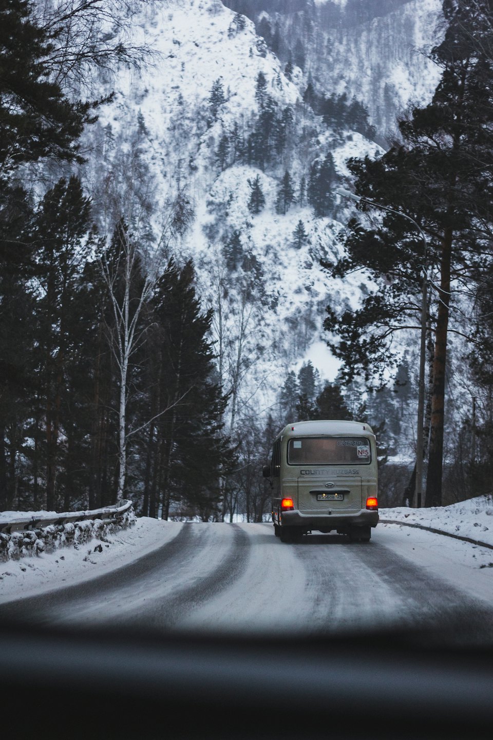 En buss kjører langs en snødekt vei gjennom en skog.